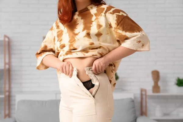 Image of woman trying to do her trousers up after pregnancy weight gain West End